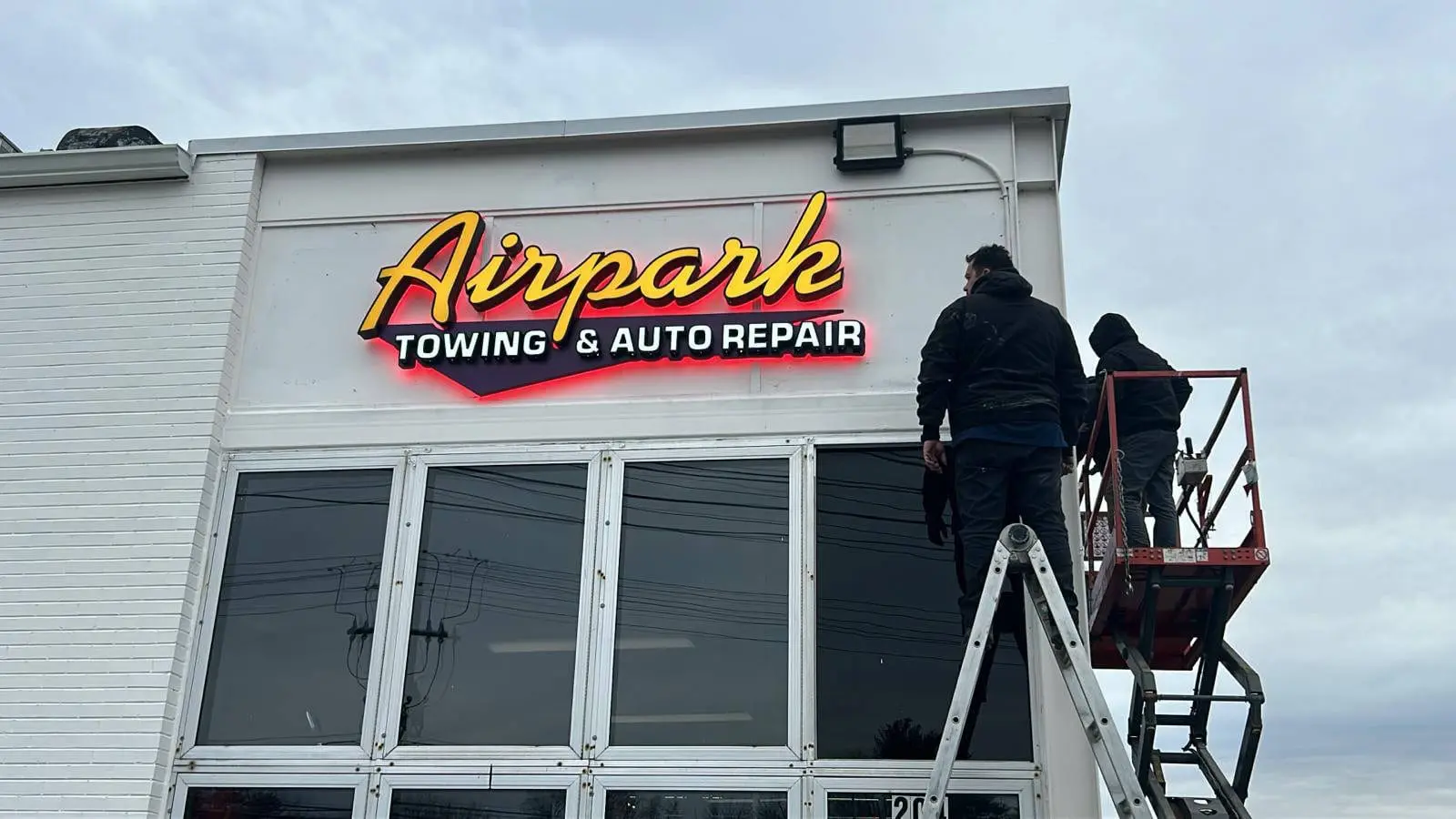Installers fitting a halo-lit sign for Airpark Towing & Auto Repair