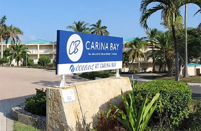 Eingangsschild des Carina Bay Resort auf einem Steinsockel zwischen Palmen