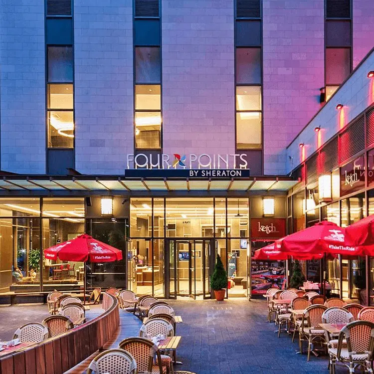 Eingang des Four Points by Sheraton mit beleuchteten Fassadenbuchstaben in der Abenddämmerung