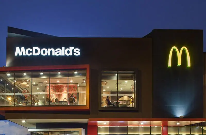 Fachada de un restaurante McDonald's con logotipo y letras iluminados al anochecer