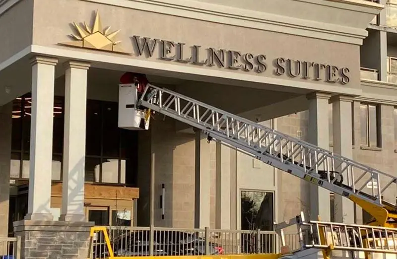 Montage der Buchstaben von Wellness Suites am Eingang einer Wohnanlage von einer Hebebühne aus